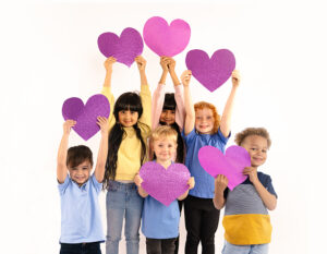 Full size photo of sweet small blond hair girl hold heart wear shirt jeans sneakers isolated on yellow background.