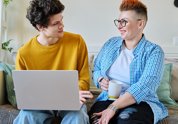 Young man with laptop sitting on couch with counsellor or psychologist
